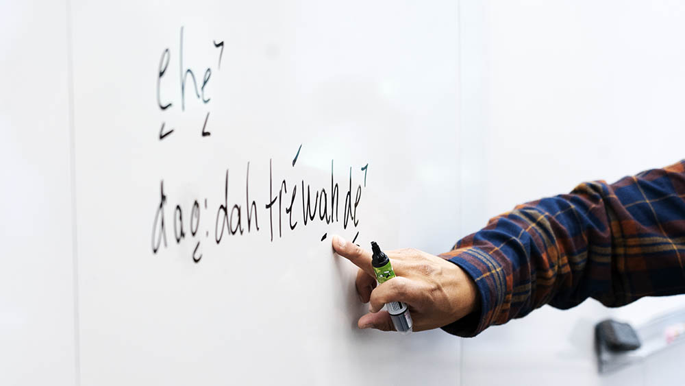 Hand pointing to words written in the language of the Cayuga Nation on a whiteboard