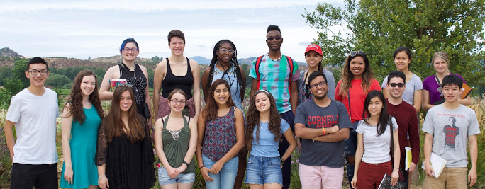 Two rows of students wearing summery clothes facing the camera with hills in the background.
