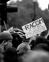 In a crowd a sign can be read saying Racism is the Pandemic