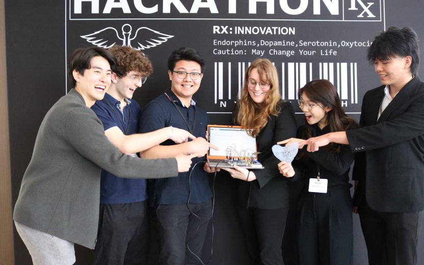 A team of Cornell students smile and laugh while pointing at a medical device held by a student in the center. 