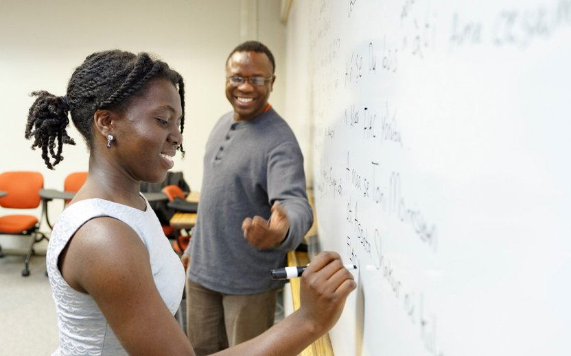 Student and teacher working at white board in classroom.
