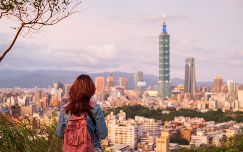 Student viewed from behind looking at Taipei cityscape at sunset.