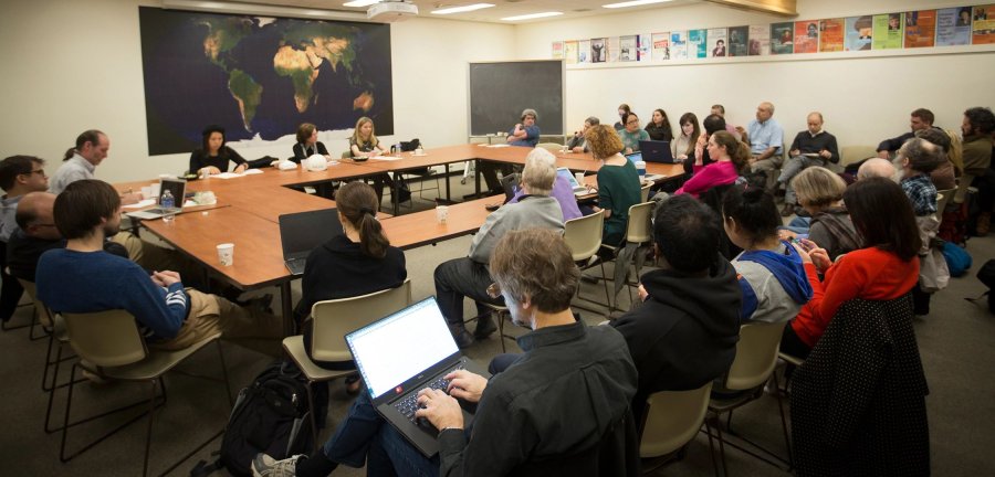 Faculty and students sitting around a square table with additional rows of seats on two sides.