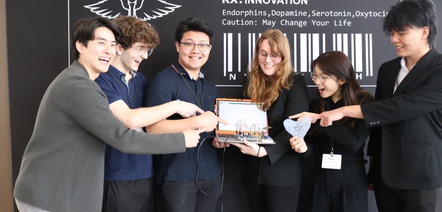 A team of Cornell students smile and laugh while pointing at a medical device held by a student in the center. 