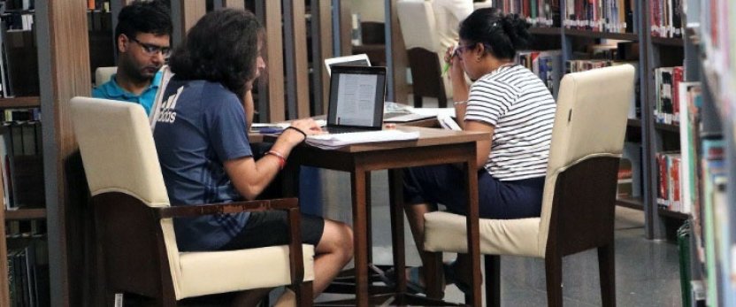 Three people sitting around a table in a library. 