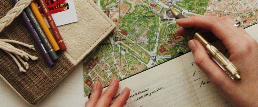 Person making a list in a notebook that is sitting on top of a map.