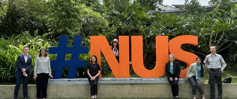 Seven Cornell faculty and staff stand around a large cutout sign that says #NUS.