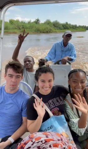 Eva Telesca and fellow study abroad students smile and wave while sitting in a boat on a river in Zambia. 