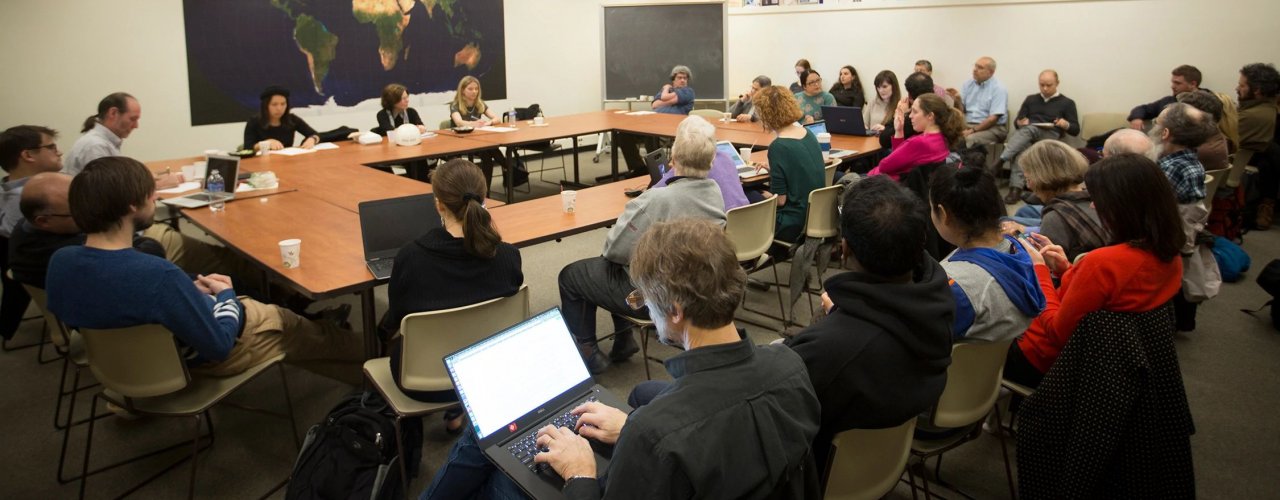 Faculty and students sitting around a square table with additional rows of seats on two sides.