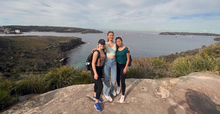 Three students standing on a hill overlooking the ocean and the city in the distance.