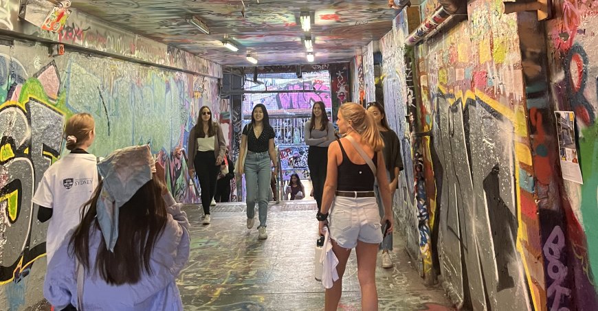 Students walking through a tunnel that is graffitied floor to ceiling. 