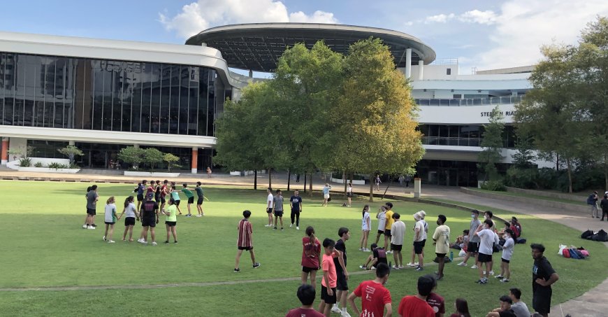 Students on a lawn on the NUS campus with buildings in the background