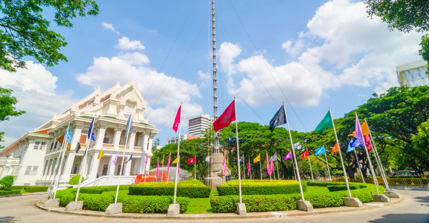 A circle of shorter flags surrounding a taller flag post with a while-columned building in the background.