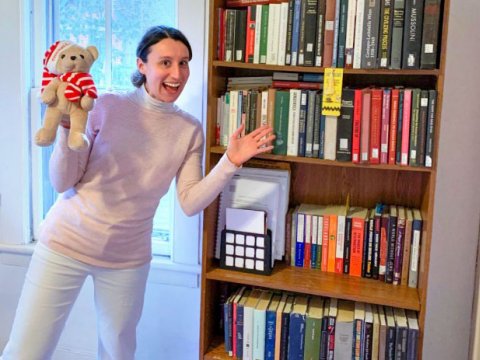 Woman holding a teddy bear in from of a full book shelf