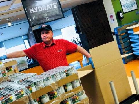 Man in red shirt and baseball cap, packing boxes of canned food