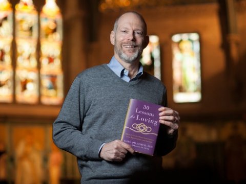 Man standing in a chapel with stained glass windows, holding a book
