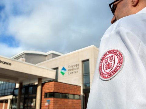 Man in wearing shirt with Cornell seal on the sleeve eking towards hospital