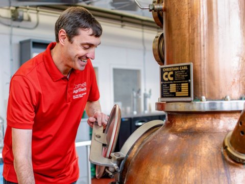 Man in red shirt opening the hatch on a distilling equipment