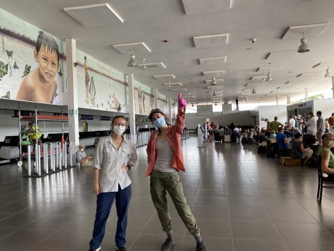 Two women wearing masks standing in an airport corridor.