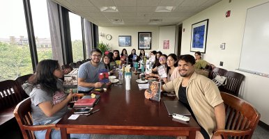 A group of students at Summer Pathways sit around a table, smiling and holding up migration books. 