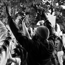 Black and white image of people standing with their hands in the air.
