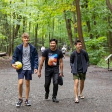 Three smiling students walking down a tree-lined path. 