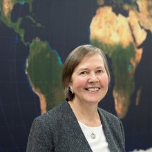 Ellen Lust smiles in front of a large map.