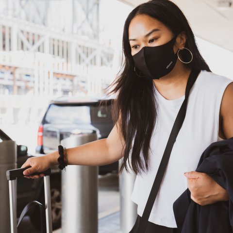 Woman traveling with luggage while wearing black face mask