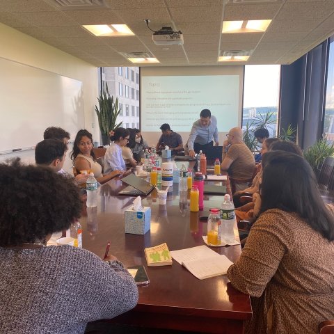 Students sit around a long rectangular table, facing a presentation on graduate school. 