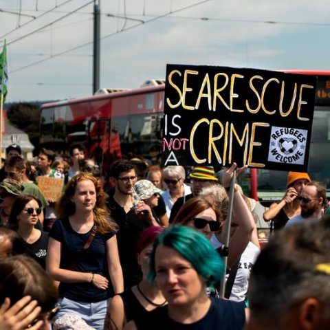 Protestors gather and hold a sign that reads, "Sea Rescue Is Not a Crime."